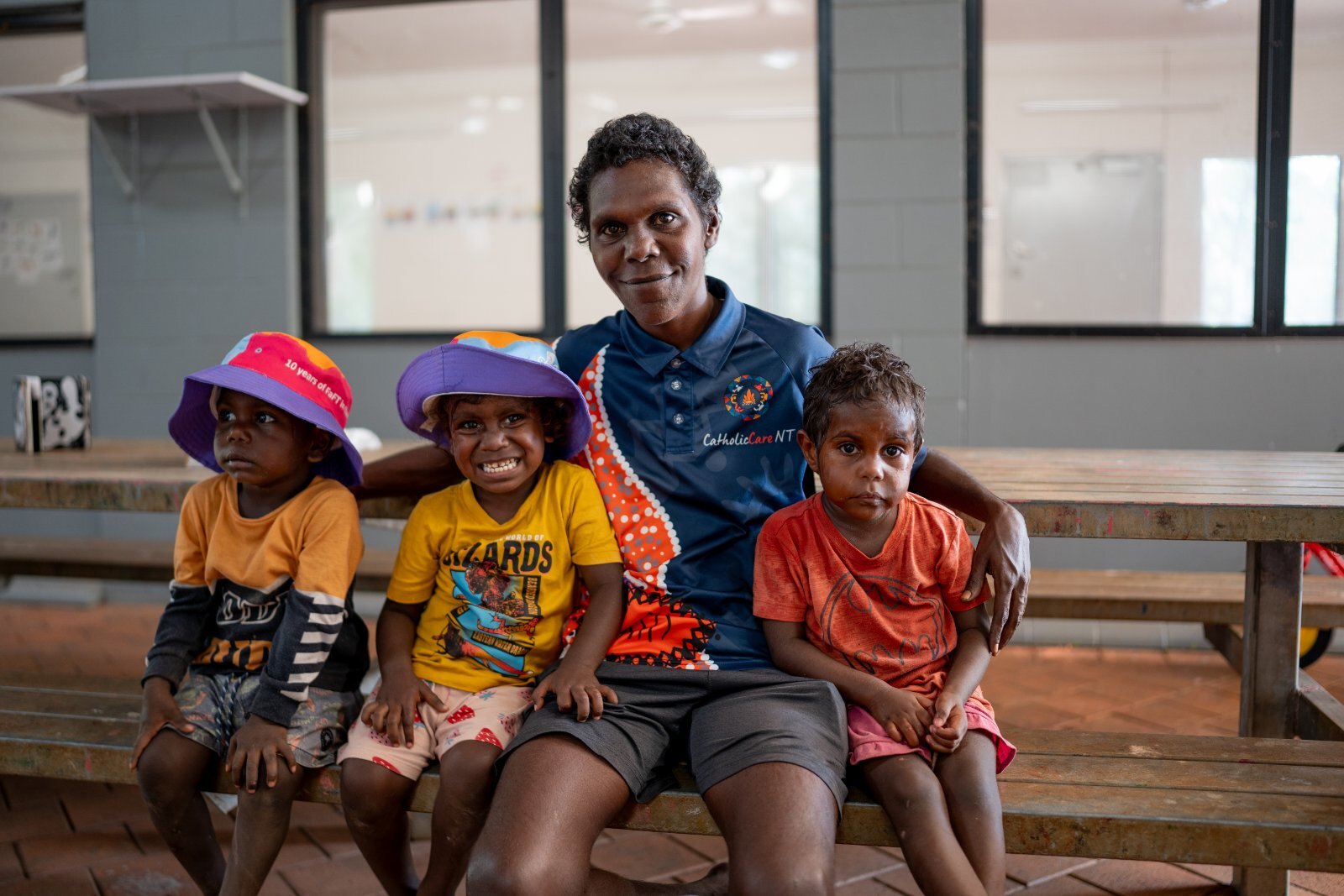 Carer with 3 children in bright clothing sitting on a school bench