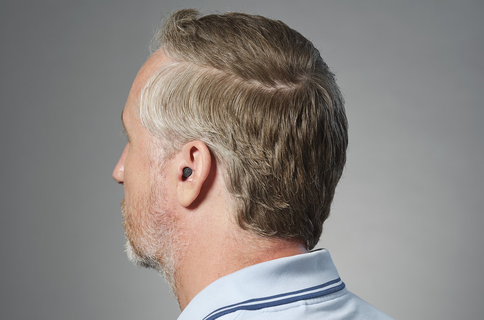 a man with grey hair and a blue shirt with a completely in the canal hearing device
