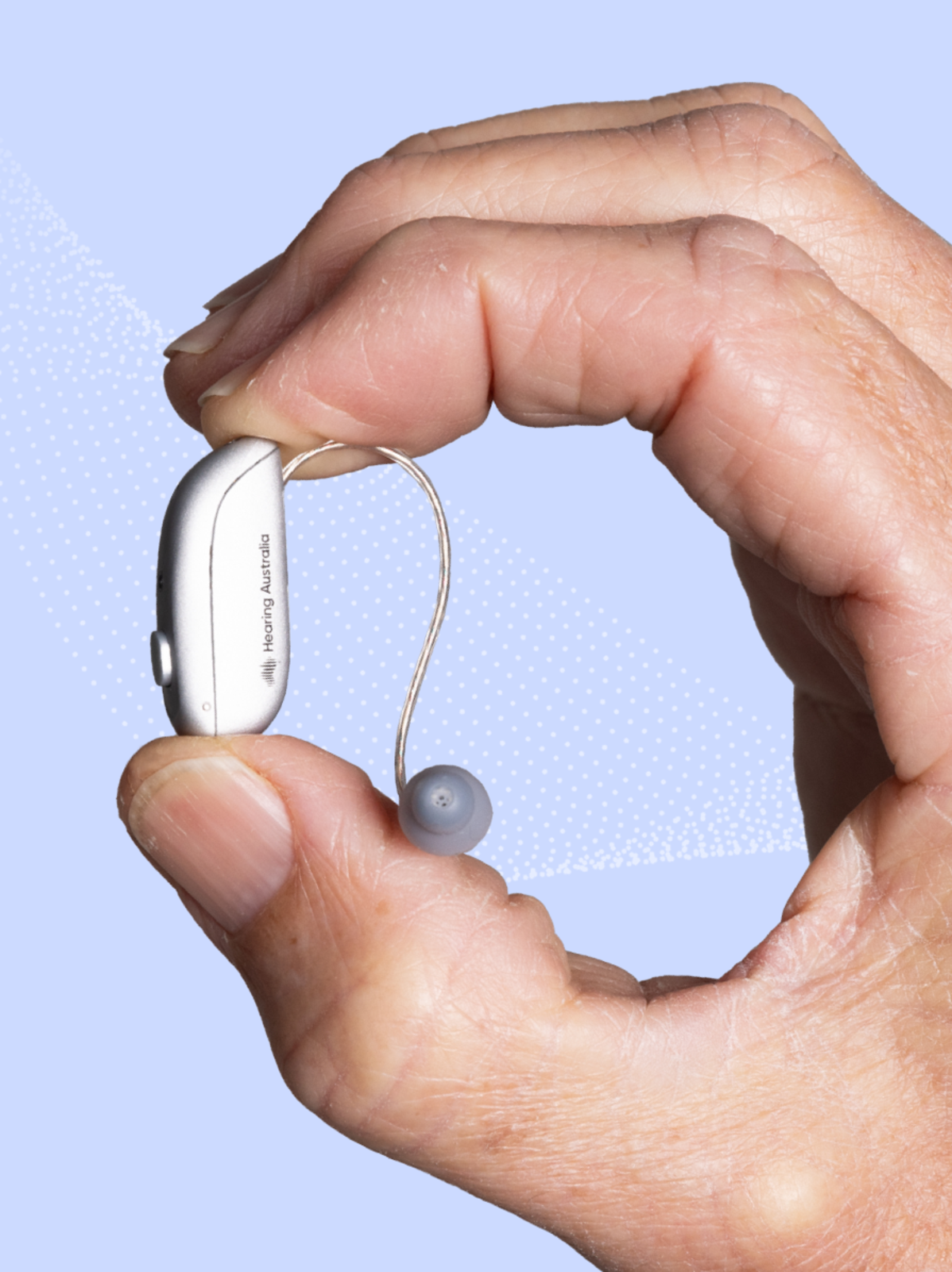 A hand holds a small Hearing Australia hearing aid with an ear dome against a light blue background