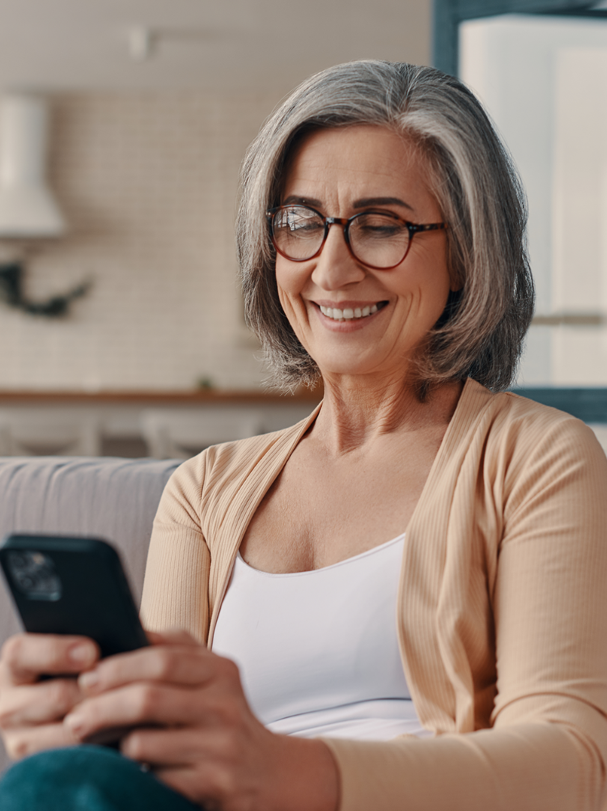 Older lady wearing glasses smiling while looking at hear smartphone